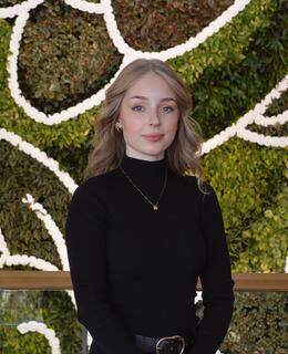 Headshot of Sasha Mathieu. Wearing black turtleneck, in front of a green forage background.