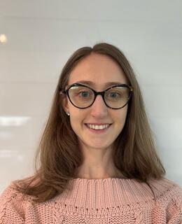 I am a woman with medium-length blonde hair, wearing dark-framed glasses and I have blue eyes. In the image, I’m wearing a pink knit sweater.