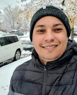 A man wearing winter gear standing on a sidewalk cover with snow