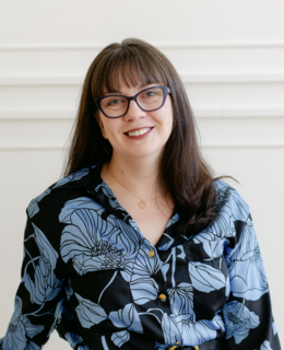 Faculty member smiling, with glasses and long brown hair wearing a blue and black floral dress. 