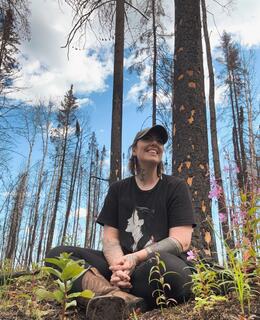Image of Andy sitting with fireweed in a recovering forest fire burn in Northern Alberta